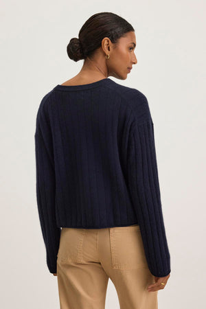 A person stands with their back to the camera, wearing the luxurious MONICA CASHMERE SWEATER by Velvet by Graham & Spencer, paired with beige pants, against a neutral background.