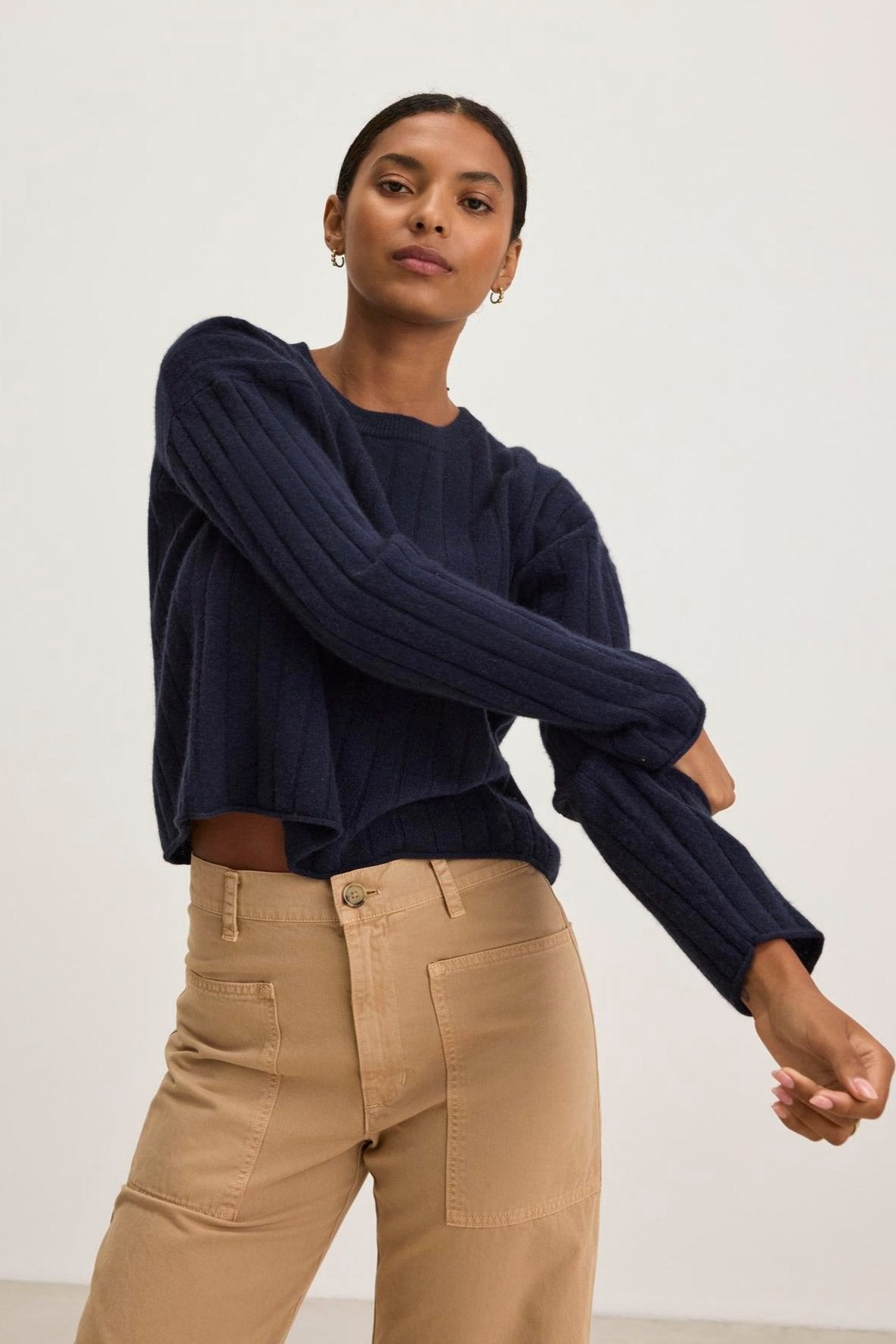   A person in a MONICA CASHMERE SWEATER by Velvet by Graham & Spencer and tan pants poses against a plain background, highlighting a wardrobe essential for those who appreciate luxury clothing. 