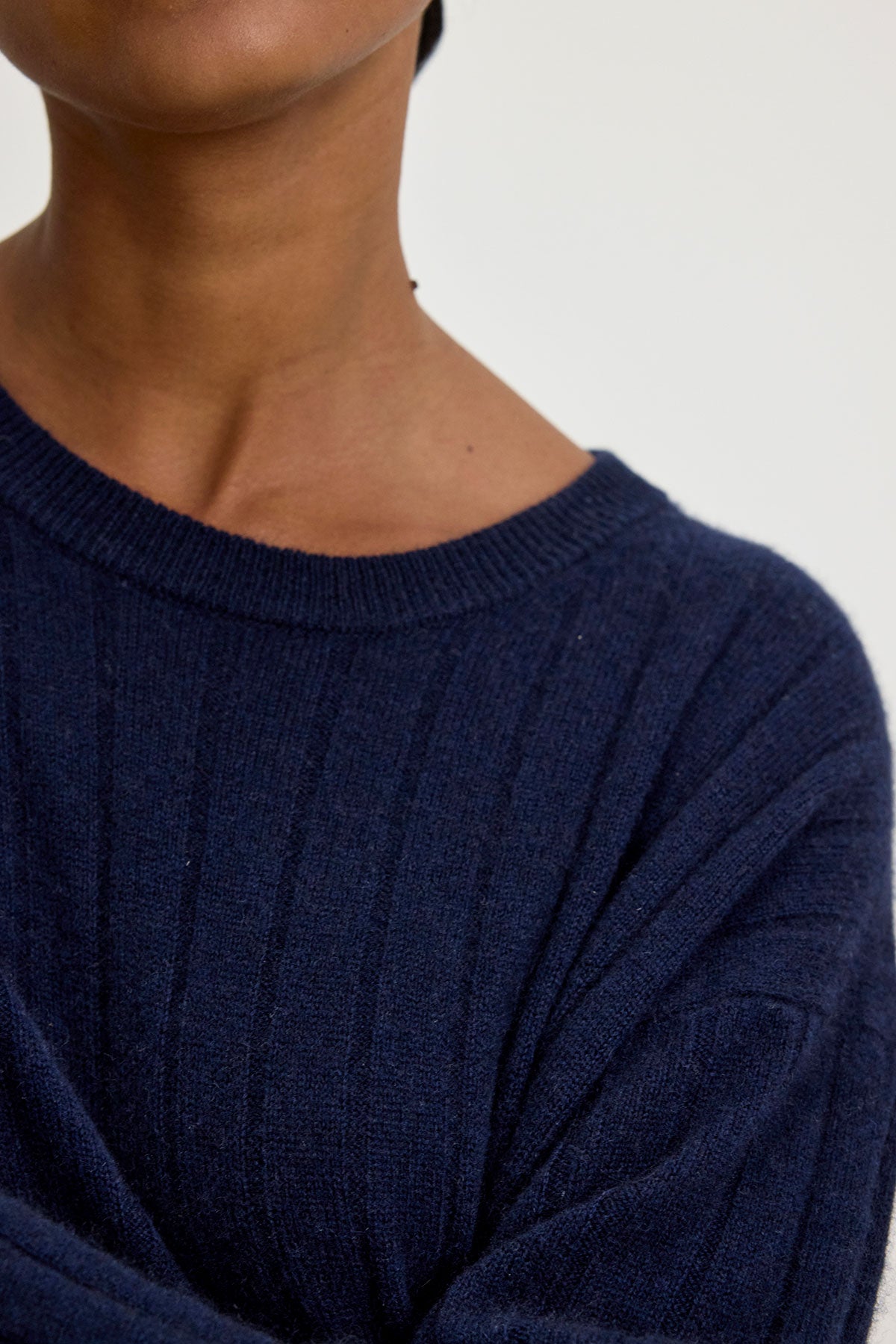 Person wearing a dark blue MONICA CASHMERE SWEATER from Velvet by Graham & Spencer, stylishly ribbed and made from 100% cashmere for luxurious comfort, seen from the shoulders up against a plain background.-37856539312321