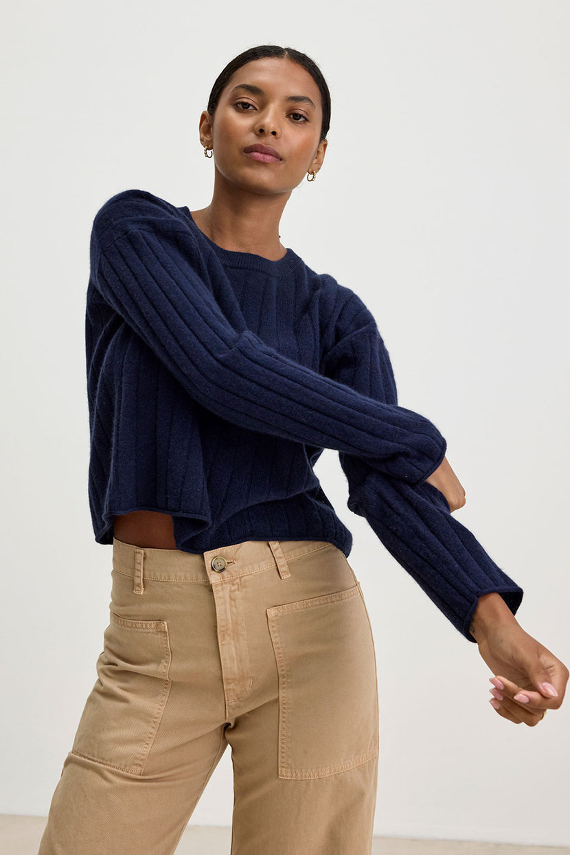 A person wearing a navy blue MONICA CASHMERE SWEATER from Velvet by Graham & Spencer, featuring the luxurious comfort of 100% cashmere, and beige pants stands against a plain background.