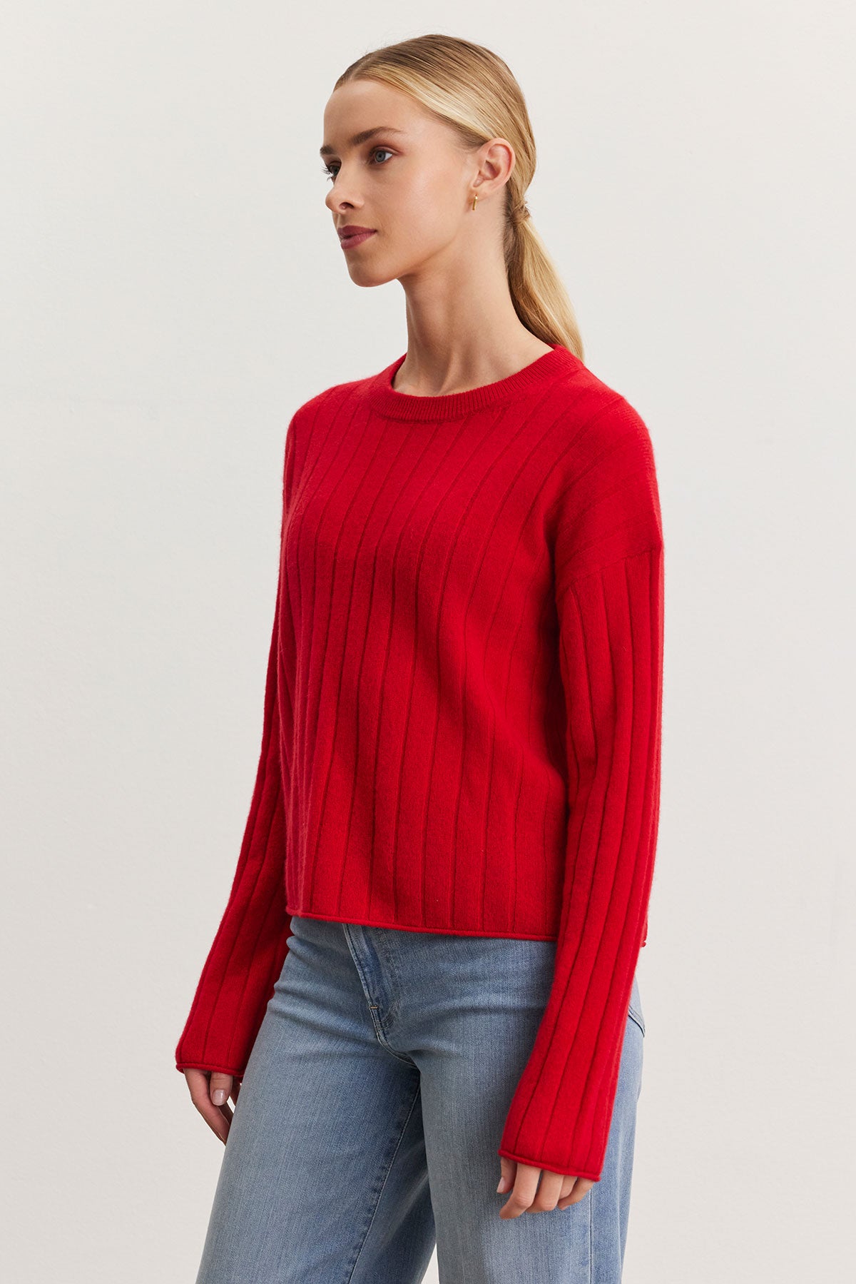   Individual dressed in a red MONICA CASHMERE SWEATER from Velvet by Graham & Spencer and blue jeans, posing against a plain backdrop. 