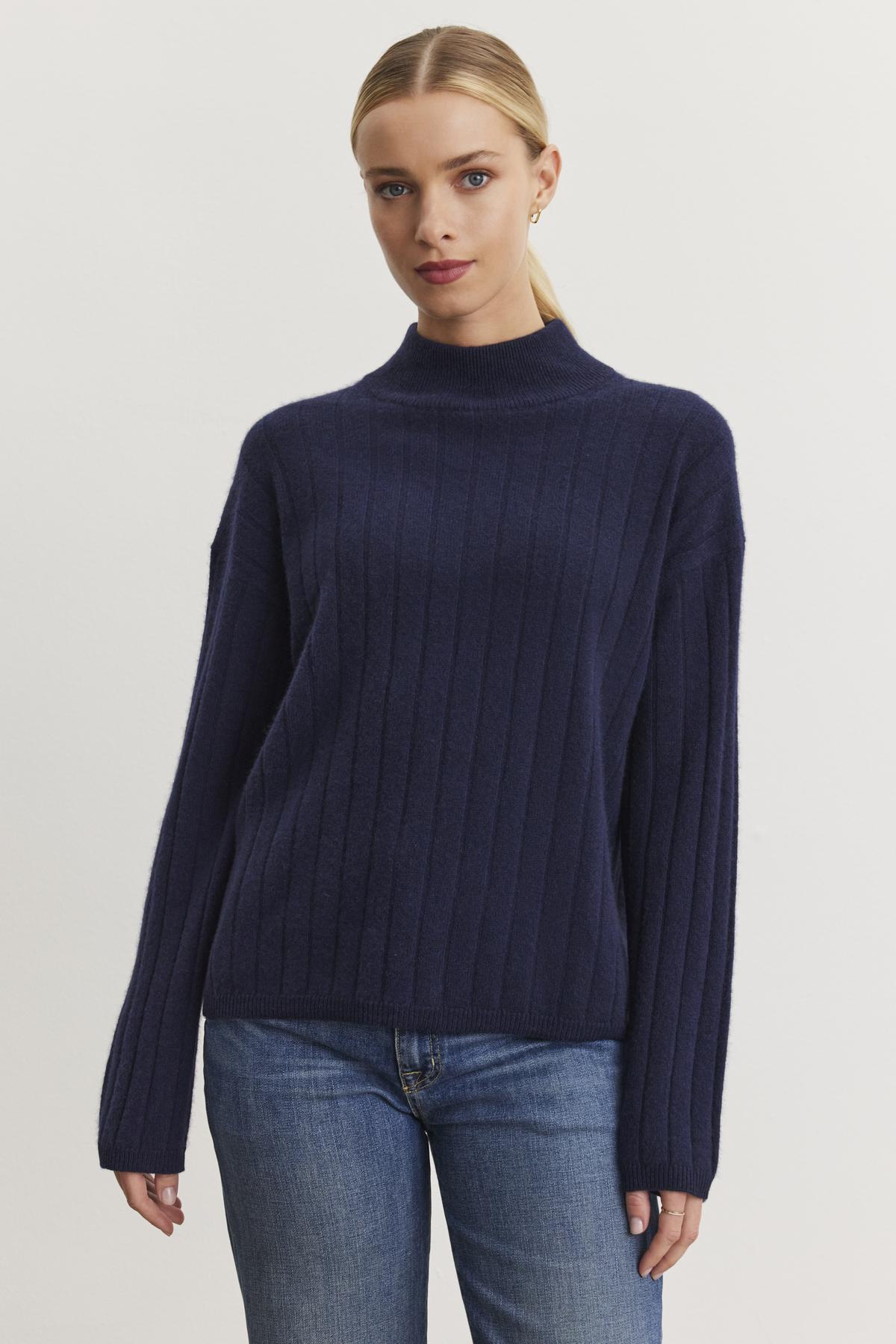   A person wearing a SIMONE CASHMERE MOCK NECK SWEATER by Velvet by Graham & Spencer and jeans stands against a neutral background. 