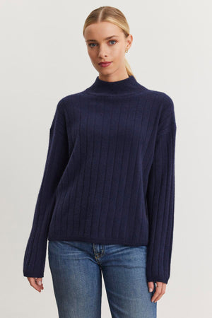 A person wearing a SIMONE CASHMERE MOCK NECK SWEATER by Velvet by Graham & Spencer and jeans stands against a neutral background.