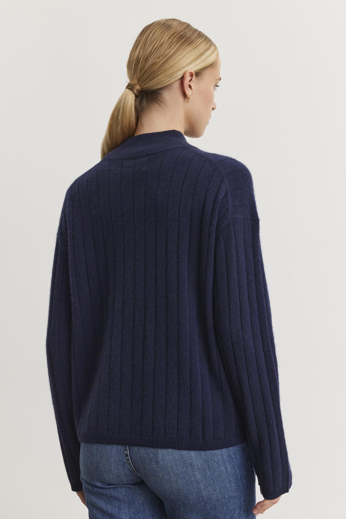   A person with long blonde hair in a ponytail is wearing the SIMONE CASHMERE MOCK NECK SWEATER by Velvet by Graham & Spencer, viewed from the back against a plain light background. 