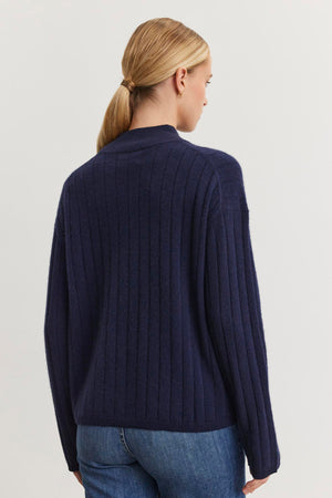 A person with long blonde hair in a ponytail is wearing the SIMONE CASHMERE MOCK NECK SWEATER by Velvet by Graham & Spencer, viewed from the back against a plain light background.