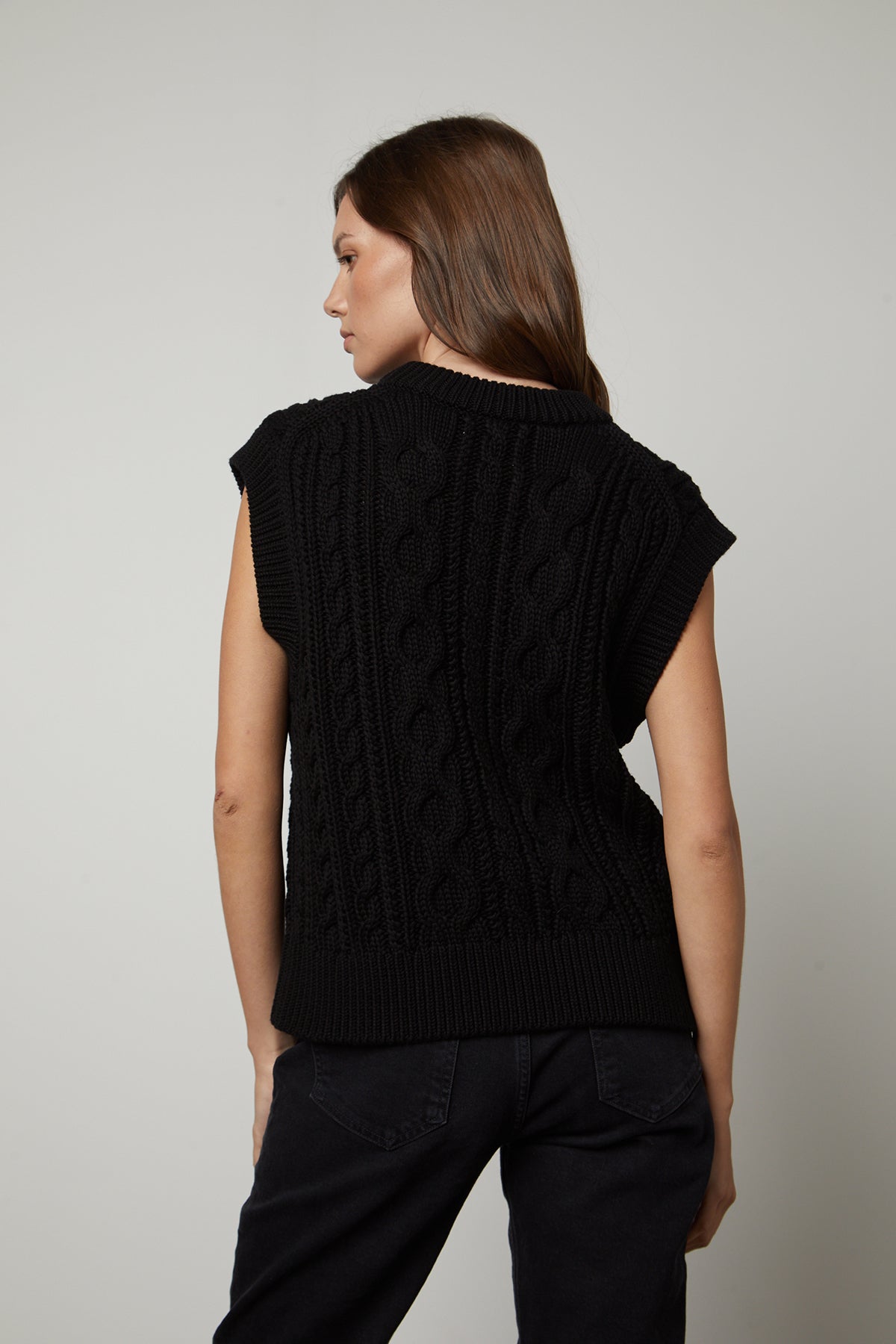 The back view of a woman wearing a black HADDEN SWEATER VEST by Velvet by Graham & Spencer.-26799841280193