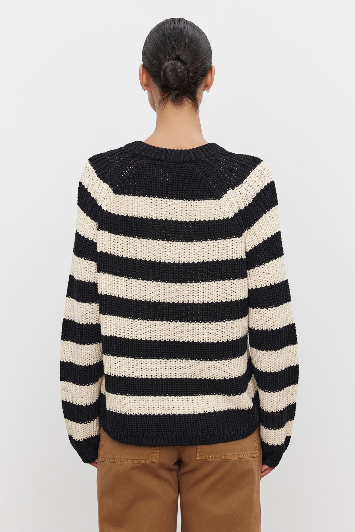   A person with their hair in a bun, wearing the black and white striped OLLIE SWEATER made of chunky pima cotton by Velvet by Graham & Spencer, paired with brown pants, viewed from the back. 