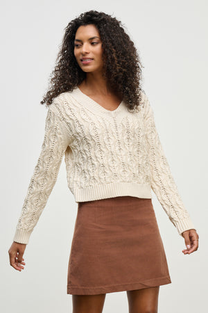 A woman wears the JOYCE SWEATER by Velvet by Graham & Spencer, a chunky Pima cotton cable knit, paired with a brown skirt against a plain light background.