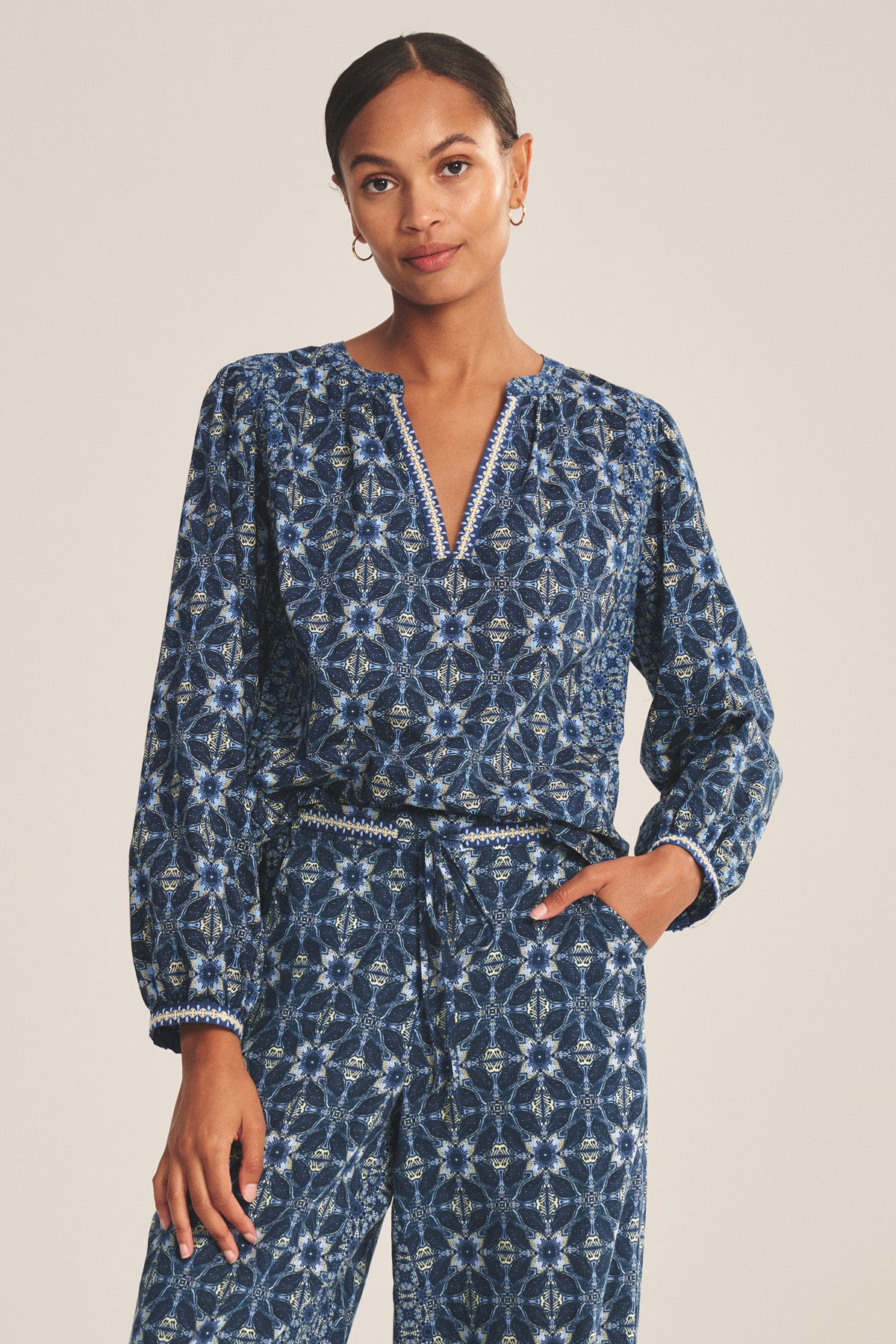 Woman wearing the CLAUDIE TOP by Velvet by Graham & Spencer— a blue printed cotton cambric top— with matching pants, standing with one hand in her pocket against a plain background.-41008182526145