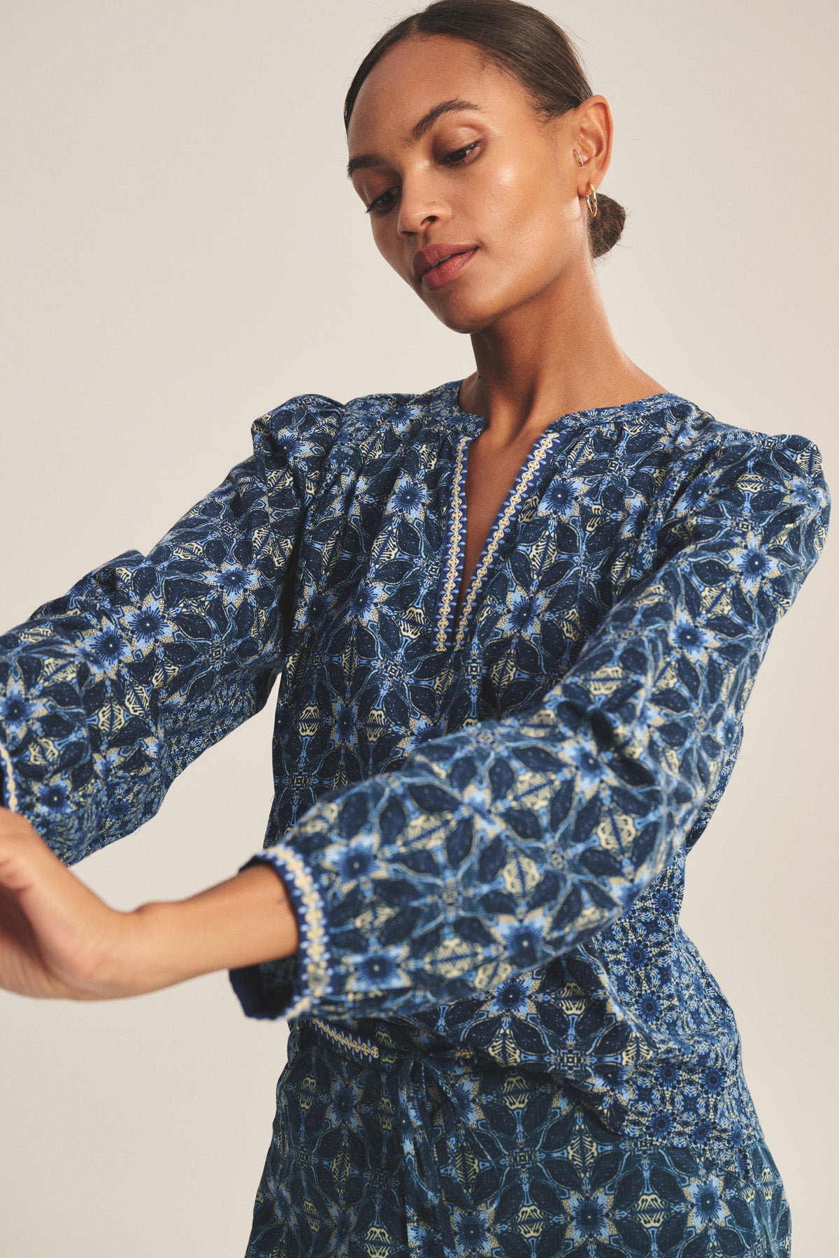 A woman wears the Velvet by Graham & Spencer CLAUDIE TOP, a blue printed cotton cambric design, paired with a matching skirt and stands with arms slightly extended against a plain background.-41008182460609