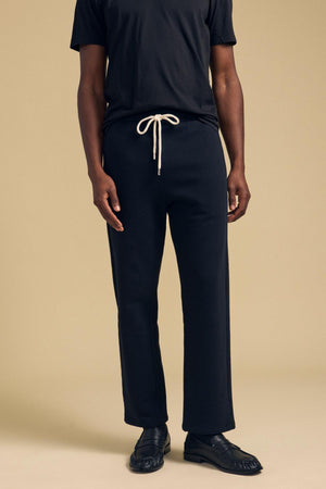 A person wearing black cotton fleece HUDSON SWEATPANT by Velvet by Graham & Spencer with a white drawstring waist and black loafers.