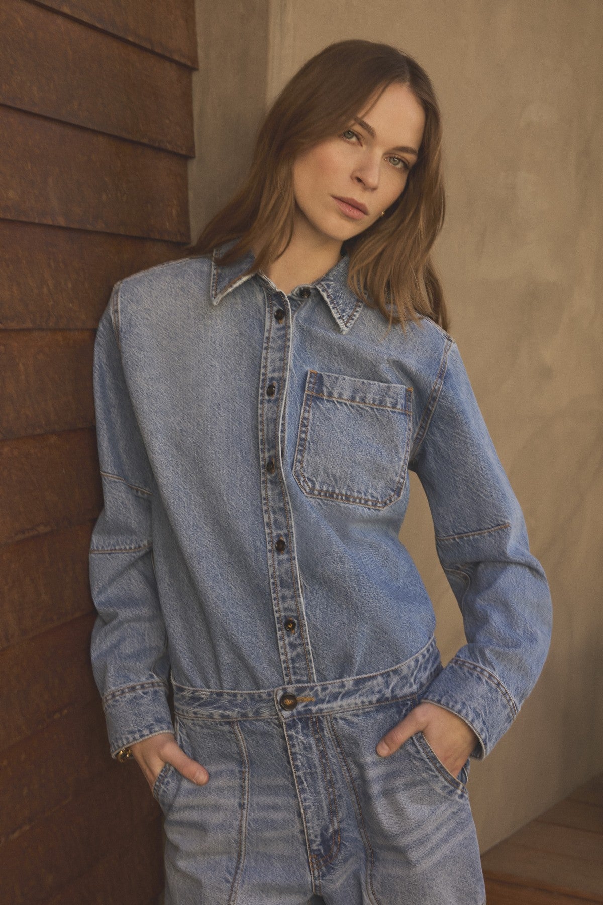 A woman with long brown hair stands indoors facing the camera, hands in her pockets, wearing the Velvet by Graham & Spencer CLEMENTINE DENIM SHIRT.-41834374725825
