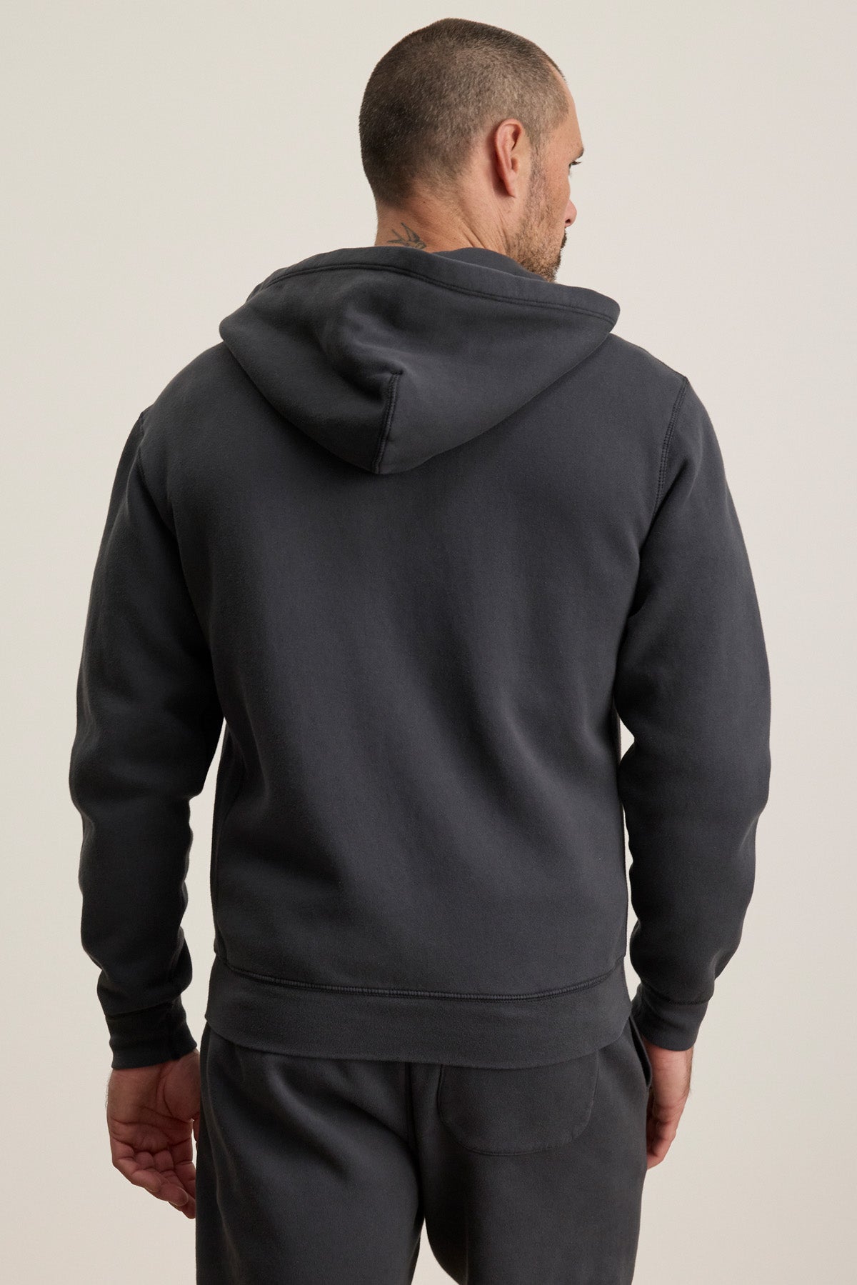 A man, seen from behind, wears the BRADFORD HOODIE by Velvet by Graham & Spencer—a dark gray full zip hoodie made from heavier-weight fleece—paired with matching sweatpants.