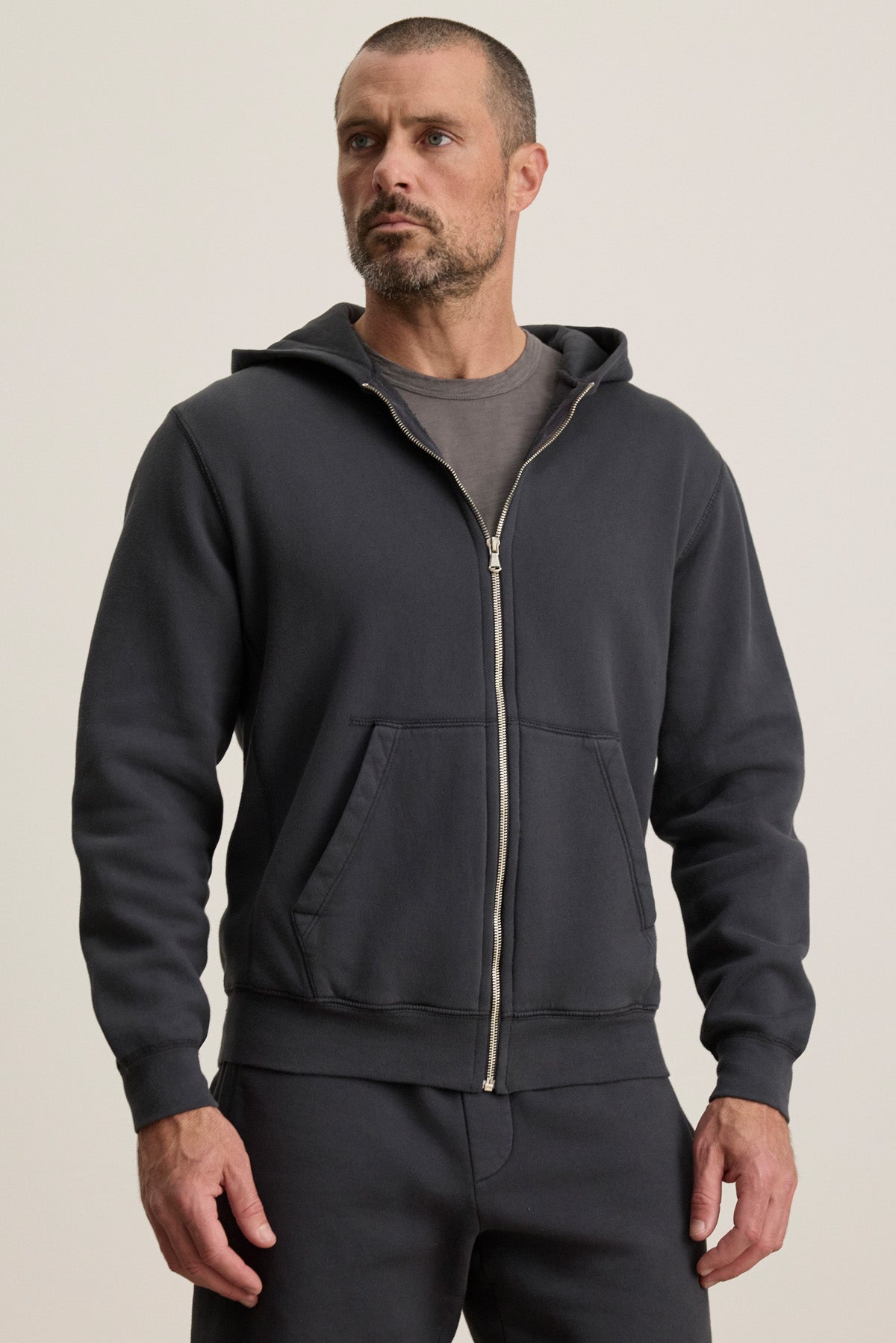 A man in the Velvet by Graham & Spencer BRADFORD HOODIE and matching pants stands against a plain light background, looking slightly to the side.-40606021255361