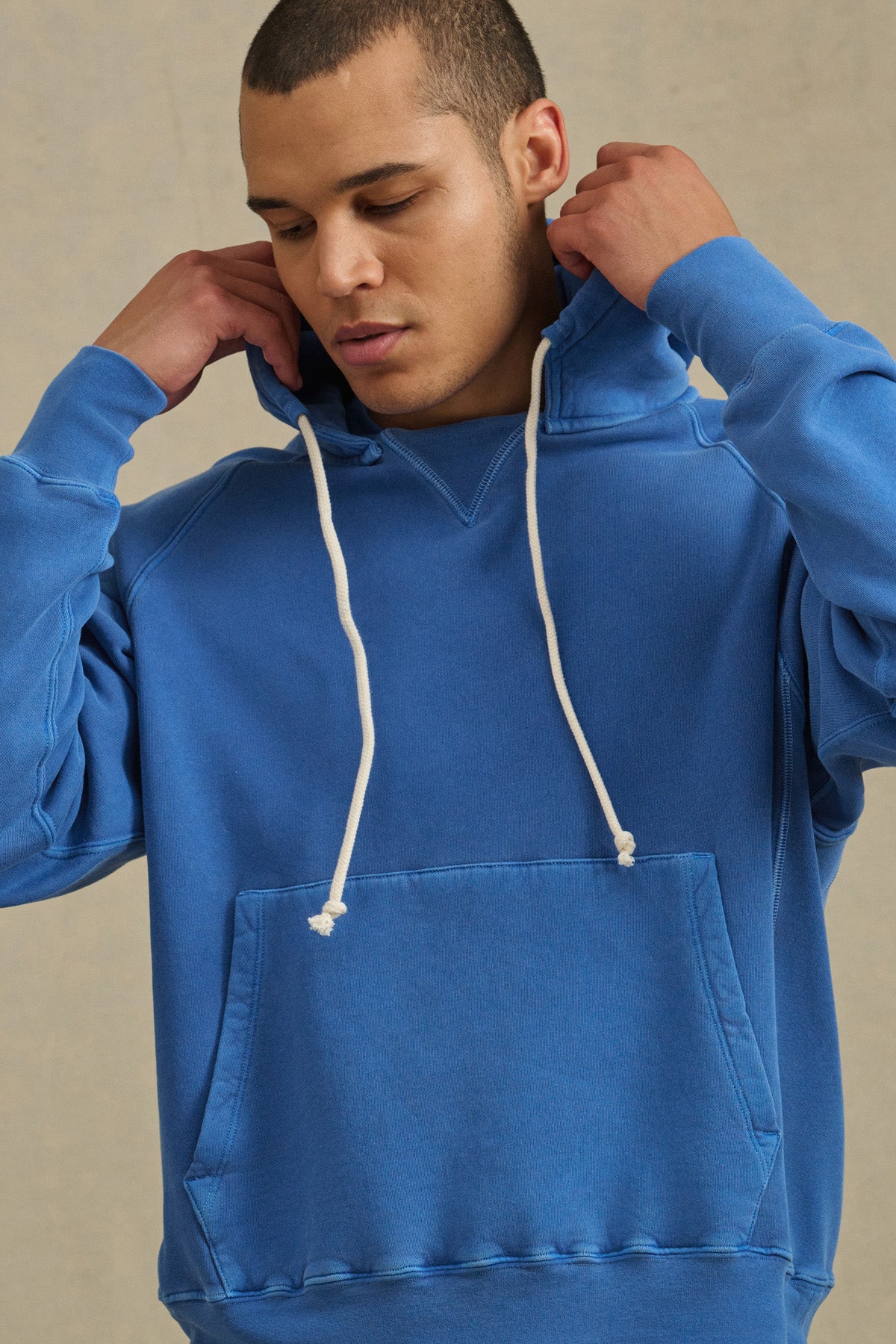 Wearing the BRODIE HOODIE by Velvet by Graham & Spencer in blue with white drawstrings, a person adjusts the hood, enjoying soft fleece and everyday comfort against a plain backdrop.-41145219612865