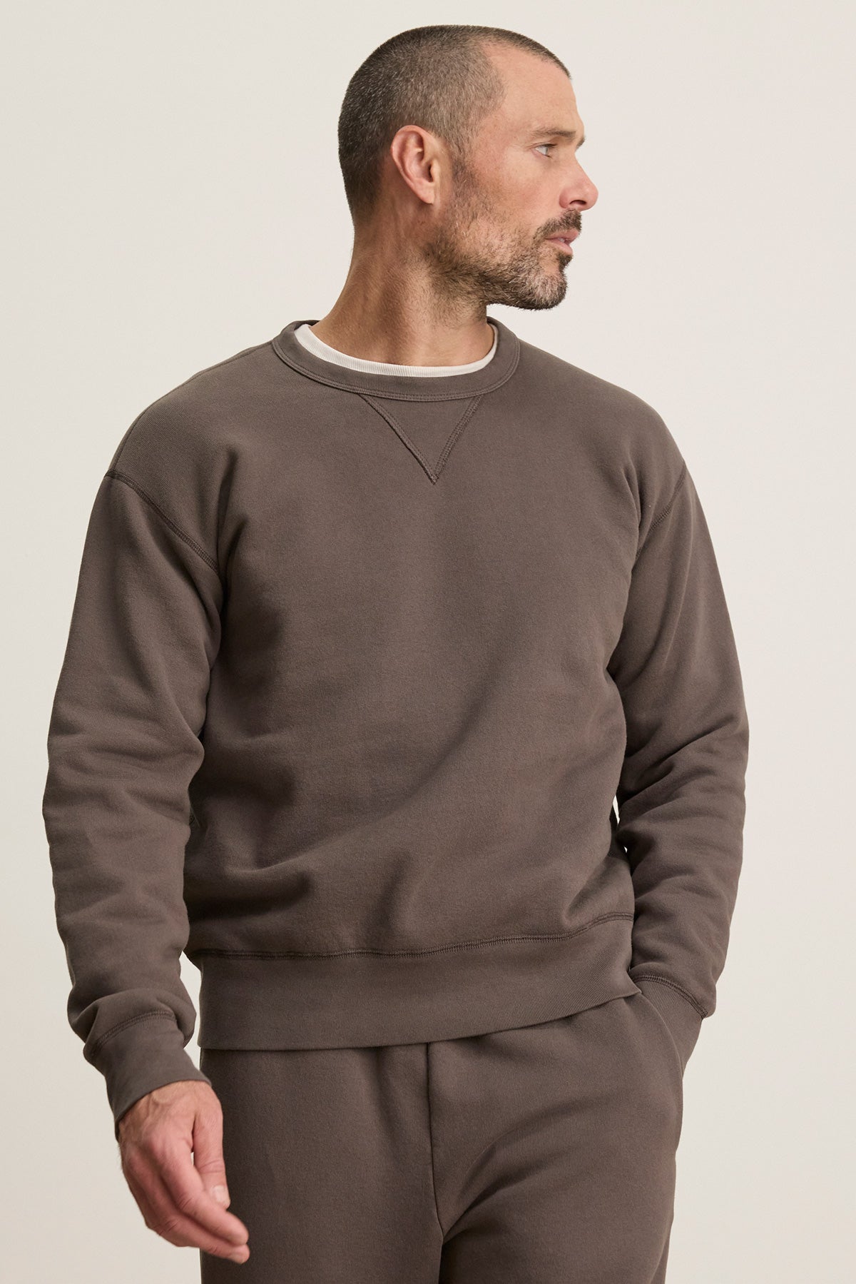 A man with short hair and a beard wears the CILLIAN SWEATSHIRT by Velvet by Graham & Spencer and matching pants, looking to his right against a plain background.-40277059371201