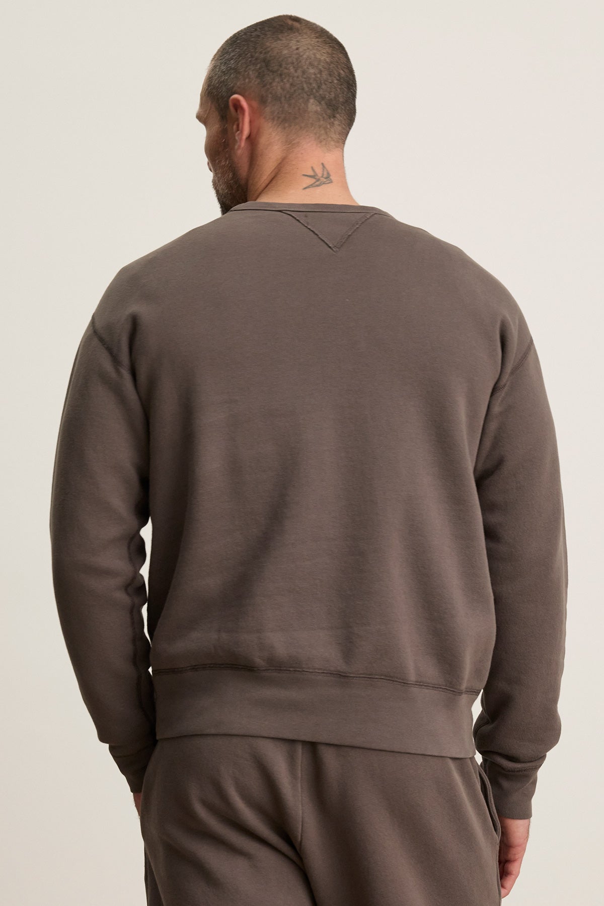 A man with short hair and a bird tattoo on his neck is seen from behind wearing the CILLIAN SWEATSHIRT by Velvet by Graham & Spencer, styled in a relaxed fit with matching pants.-40277059403969