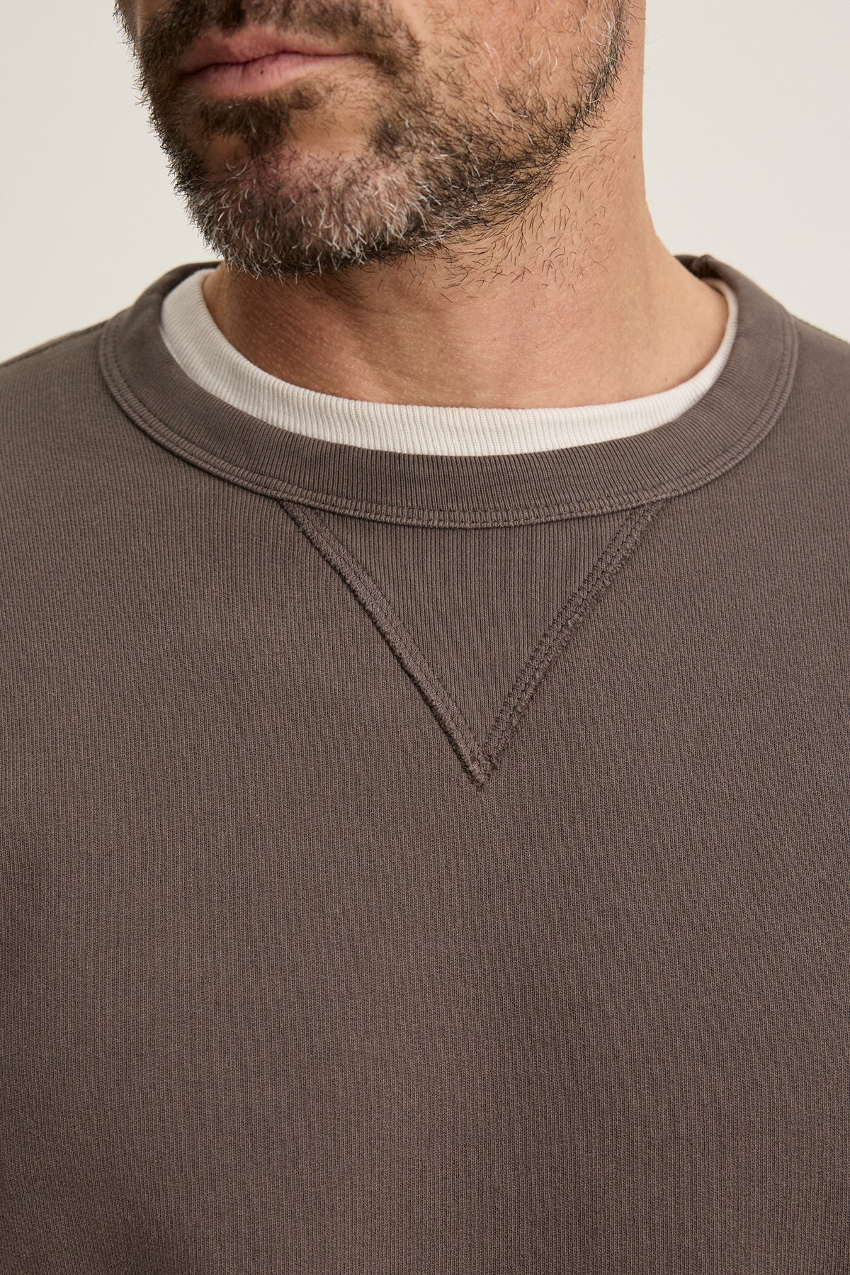 Close-up of a man with a beard wearing the CILLIAN SWEATSHIRT by Velvet by Graham & Spencer in brown, layered over a white t-shirt.-40277059338433