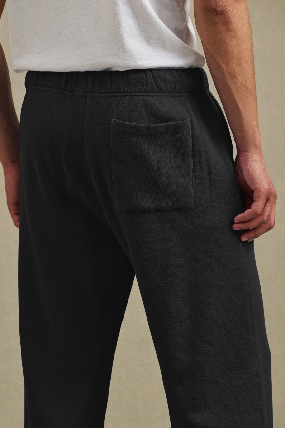 Model wears Velvet by Graham & Spencer HARLAND SWEATPANT in black, featuring a drawstring elastic waist, back pocket, and midweight fleece. Paired with a white t-shirt and photographed from behind, waist down.-40850732581057