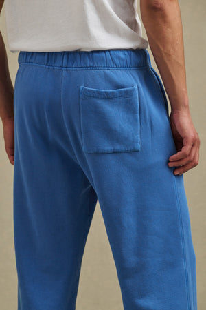 A person is seen from behind wearing Velvet by Graham & Spencer's HARLAND SWEATPANT in blue, a straight-leg, midweight fleece pant with an elastic drawstring waist and single back pocket, paired with a white T-shirt.