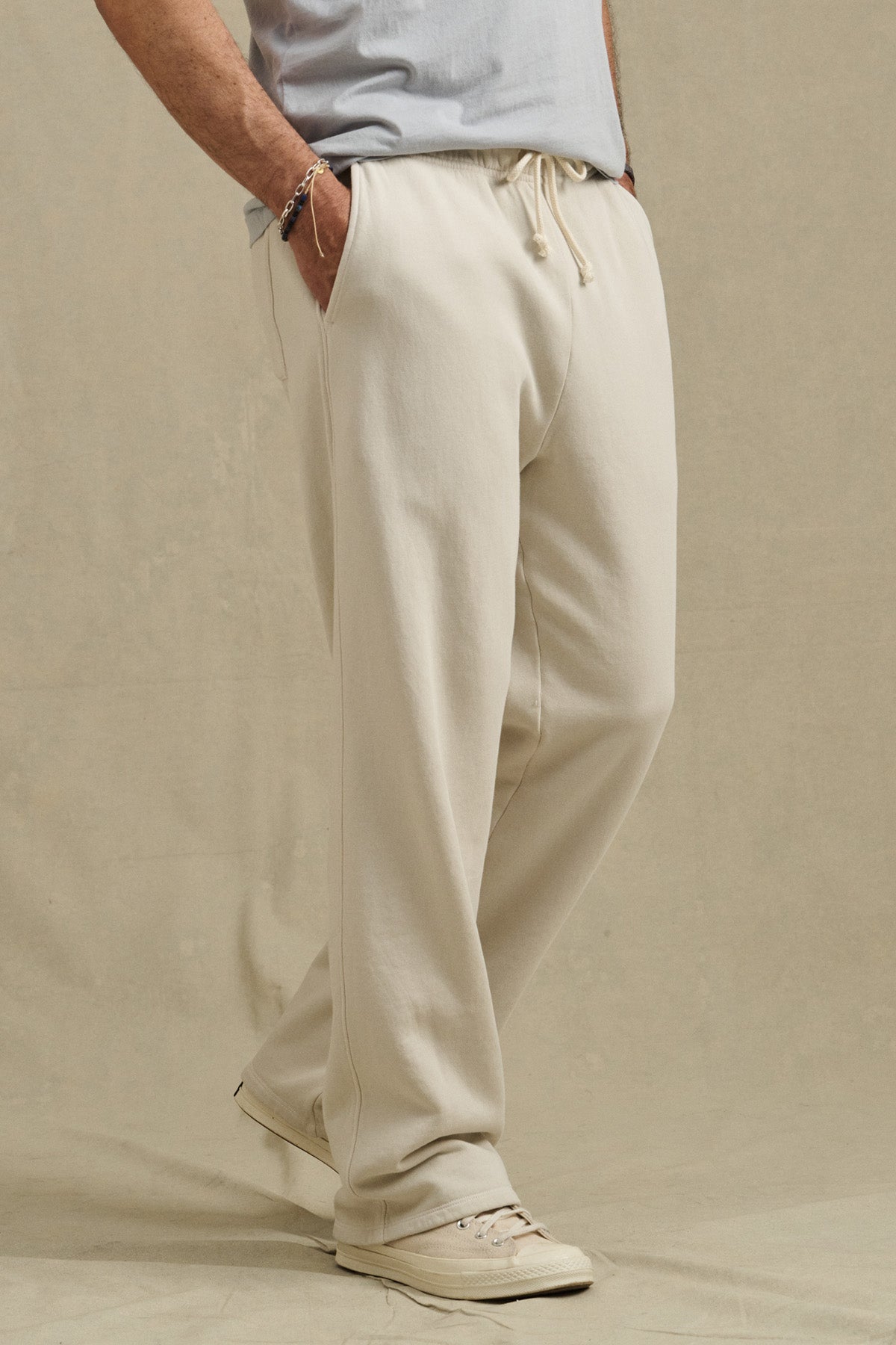 Wearing Velvet by Graham & Spencer HARLAND SWEATPANT in off-white fleece with a drawstring waist, a light grey t-shirt, and cream sneakers, a person stands hands-in-pockets against a neutral background.-40850732482753