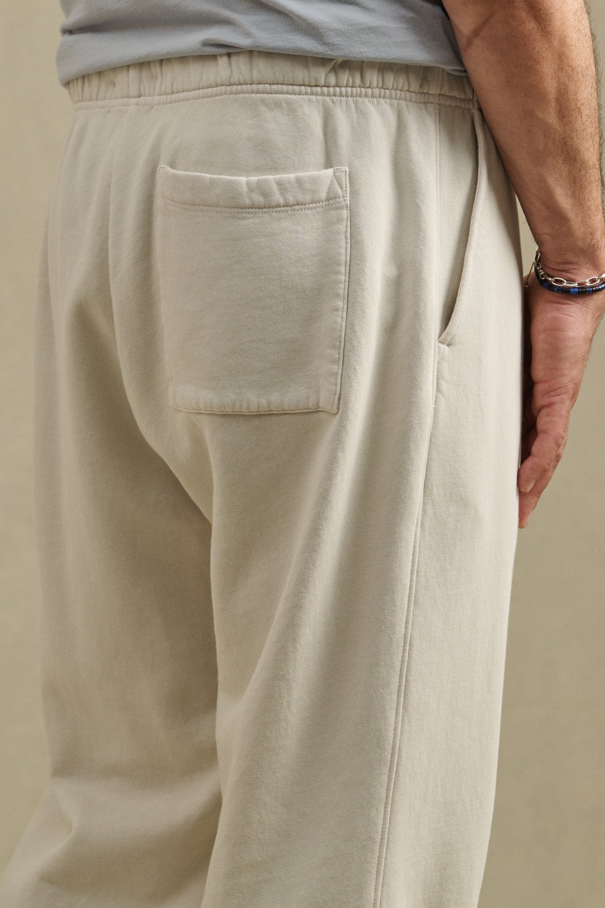 A person wearing the HARLAND SWEATPANT by Velvet by Graham & Spencer in light beige midweight fleece, featuring a drawstring elastic waist, back pocket, and side seam pocket, shown from the waist down.