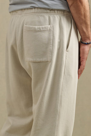 A person wearing the HARLAND SWEATPANT by Velvet by Graham & Spencer in light beige midweight fleece, featuring a drawstring elastic waist, back pocket, and side seam pocket, shown from the waist down.