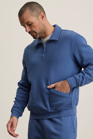 A man wearing the LEVI SWEATSHIRT by Velvet by Graham & Spencer and matching pants stands against a plain background, looking down with one hand in his front pocket.