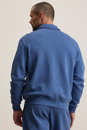 A man faces away from the camera, wearing the LEVI SWEATSHIRT by Velvet by Graham & Spencer and matching blue pants against a plain background.