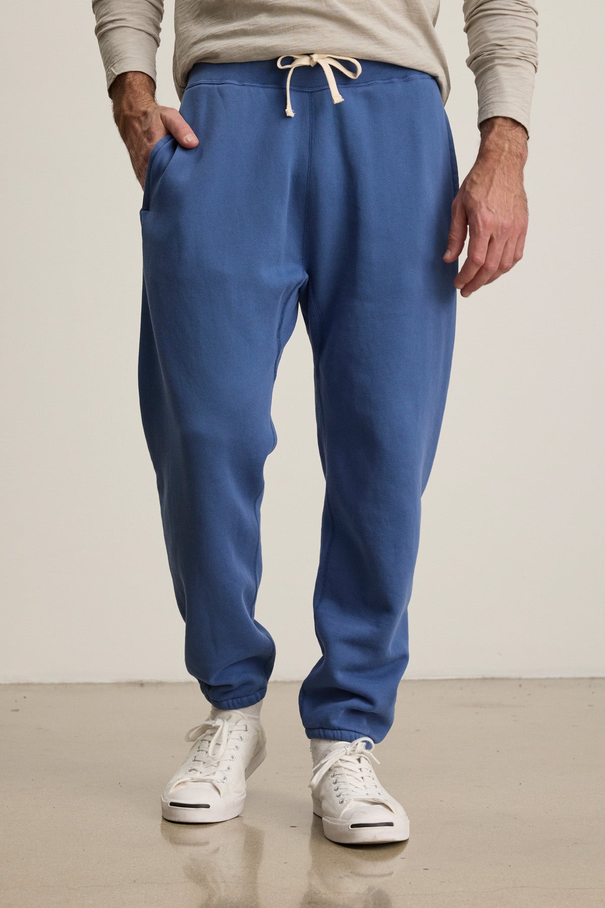 Wearing a light gray long-sleeve shirt, Velvet by Graham & Spencer's NORRIS JOGGER in blue fleece with a drawstring elastic waist, and white sneakers—ideal for everyday style on a polished floor.-40606036721857