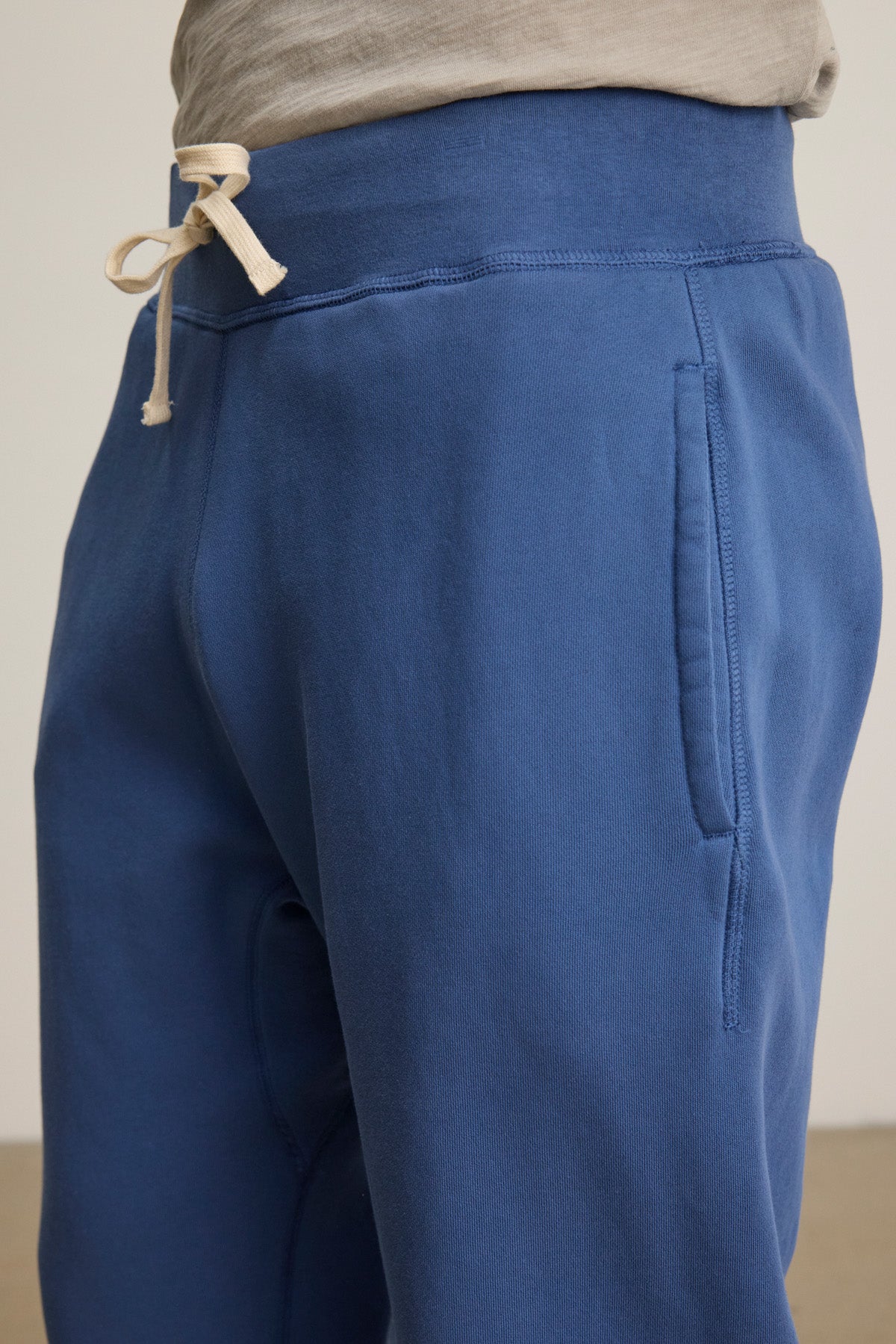 Close-up of a person wearing Velvet by Graham & Spencer's NORRIS JOGGER, blue heavyweight fleece sweatpants with a drawstring elastic waist and gray shirt—ideal for everyday wear.