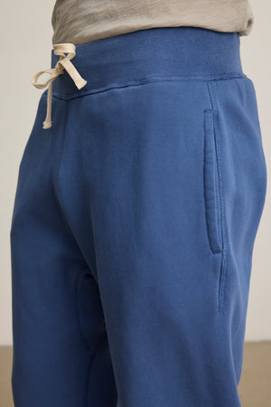 Close-up of a person wearing Velvet by Graham & Spencer's NORRIS JOGGER, blue heavyweight fleece sweatpants with a drawstring elastic waist and gray shirt—ideal for everyday wear.