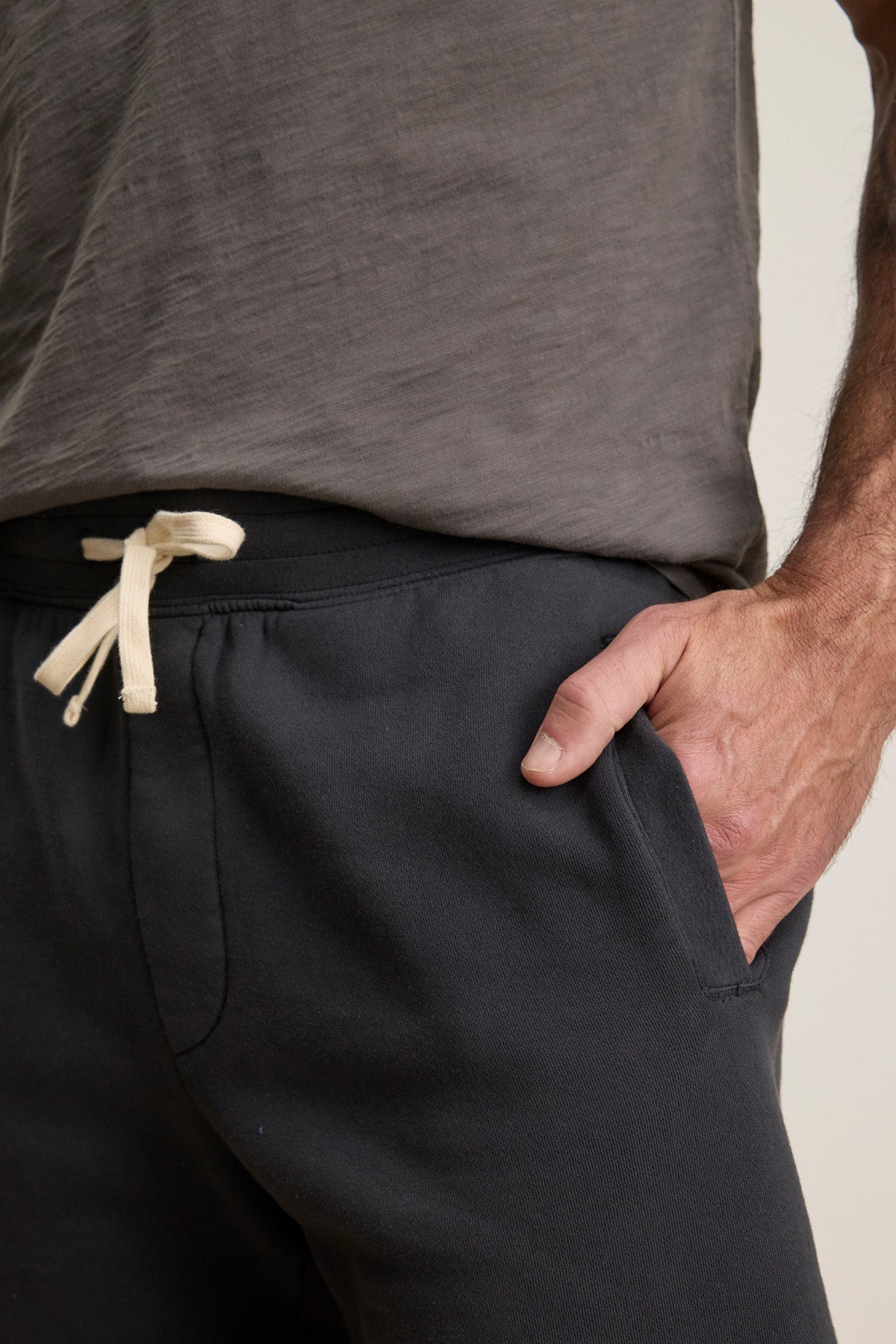 A person wearing Velvet by Graham & Spencer's RUDY SHORT—a dark lounge short with a white drawstring elastic waist—has their right hand in their pocket.