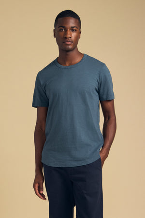 A man wearing the AMARO TEE in slate blue and dark trousers.