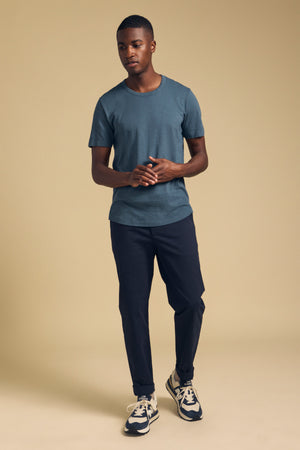 A man wearing a blue Velvet by Graham & Spencer AMARO TEE, dark trousers, and sneakers.