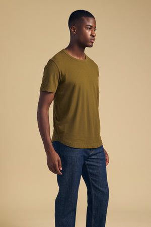 A man wearing an olive green short-sleeved AMARO TEE by Velvet by Graham & Spencer and blue jeans.