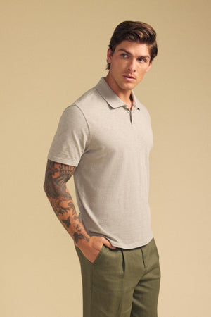 A man wearing the Velvet by Graham & Spencer MORRIS POLO in light gray cotton slub and olive green pants stands with one hand in his pocket against a beige background.