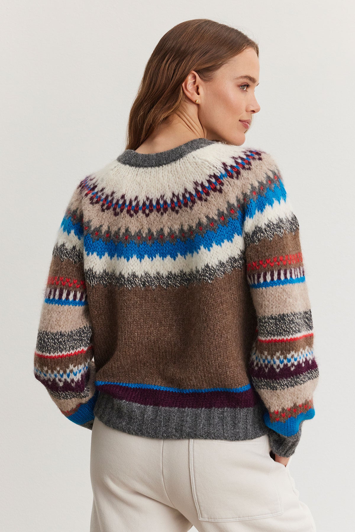   A person wearing the KELLA ALPACA FAIR ISLE SWEATER by Velvet by Graham & Spencer, featuring multicolored geometric patterns, facing slightly to the side. 