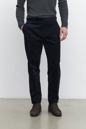 A person standing, wearing a dark gray long-sleeve shirt, the KRYSTOF CORDUROY PANT by Velvet by Graham & Spencer, and dark brown shoes.