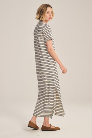 A woman in the CORIN DRESS by Velvet by Graham & Spencer, a yarn-dyed stripe jersey T-shirt dress, pairs it with brown loafers and stands sideways against a plain background.