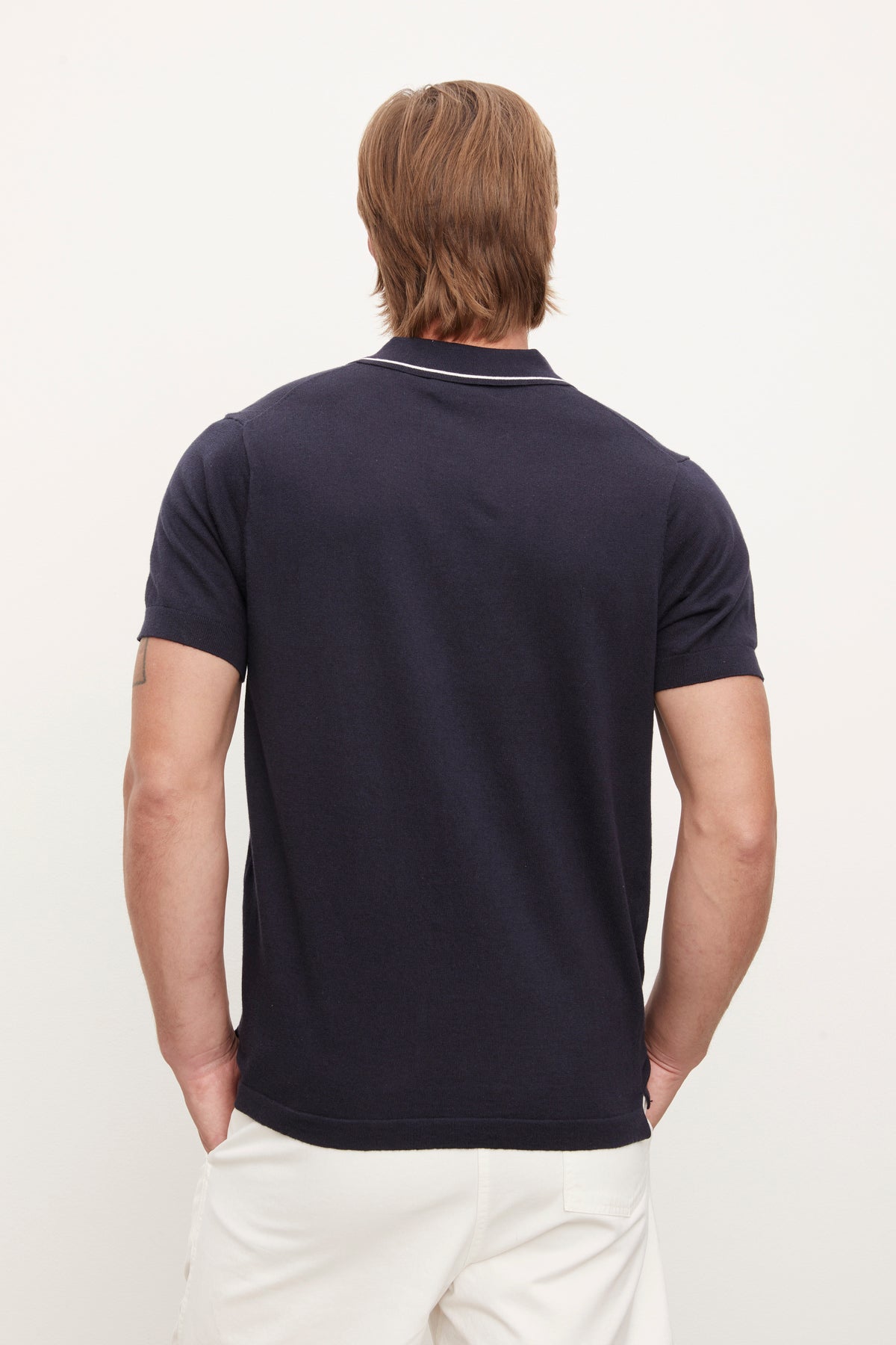Man wearing a Velvet by Graham & Spencer Shepard Polo shirt in navy blue and white pants, standing with his back to the camera, against a white background.-36753534812353