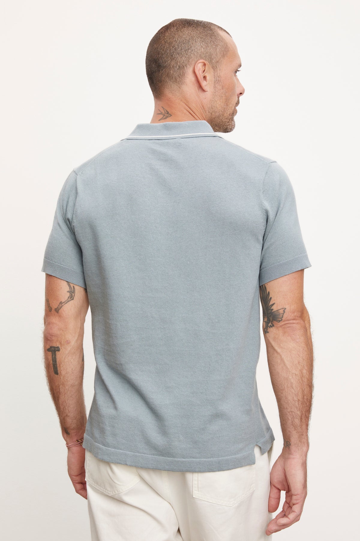 A man viewed from behind, wearing a Velvet by Graham & Spencer Shepard polo shirt in light blue and white pants, with visible tattoos on both arms.-36891061911745