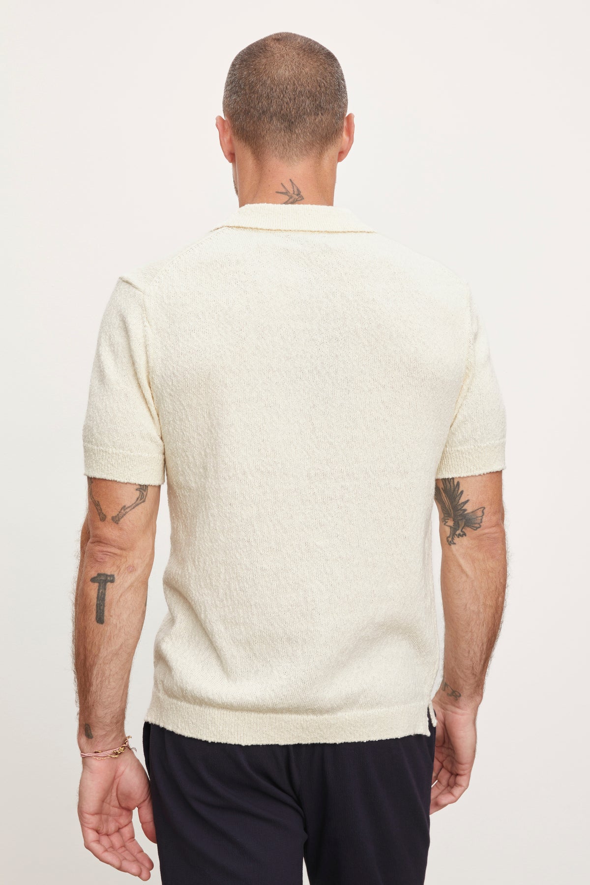   Rear view of a man with tattoos standing, wearing a Velvet by Graham & Spencer TIBERIUS POLO shirt and dark pants. 
