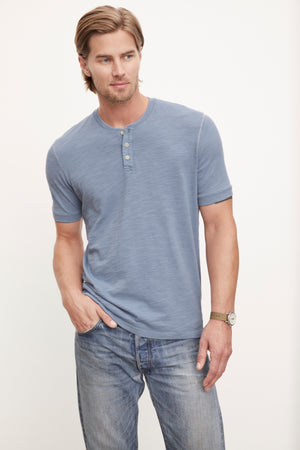 A man wearing jeans and a blue Velvet by Graham & Spencer VITO Henley t-shirt.