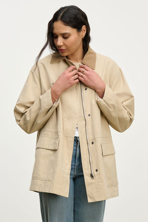 A woman buttoning the ROSA JACKET by Velvet by Graham & Spencer—an oversized cotton canvas jacket styled over a white shirt and blue jeans for a chic everyday look.