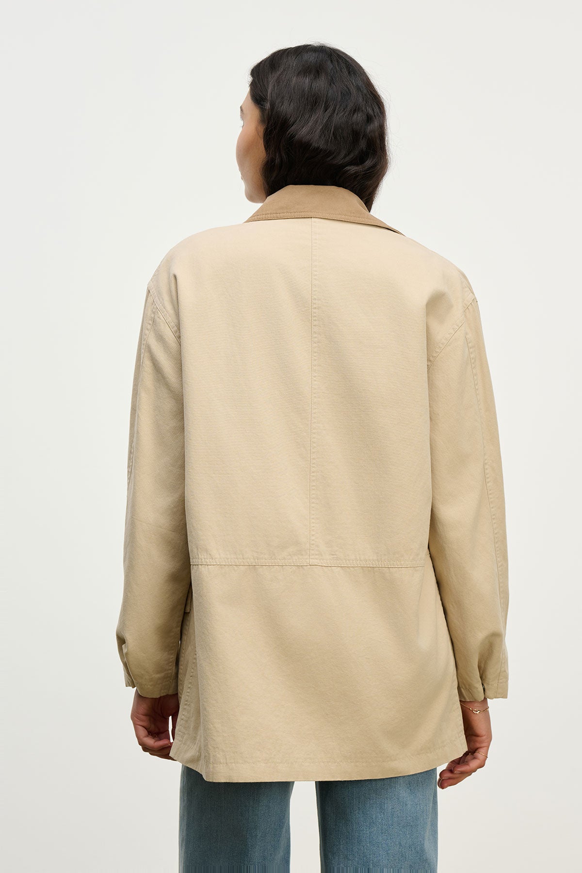 A person stands with their back to the camera in Velvet by Graham & Spencer’s oversized ROSA JACKET and blue jeans against a plain background—a stylish option for everyday wear.-39654937002177