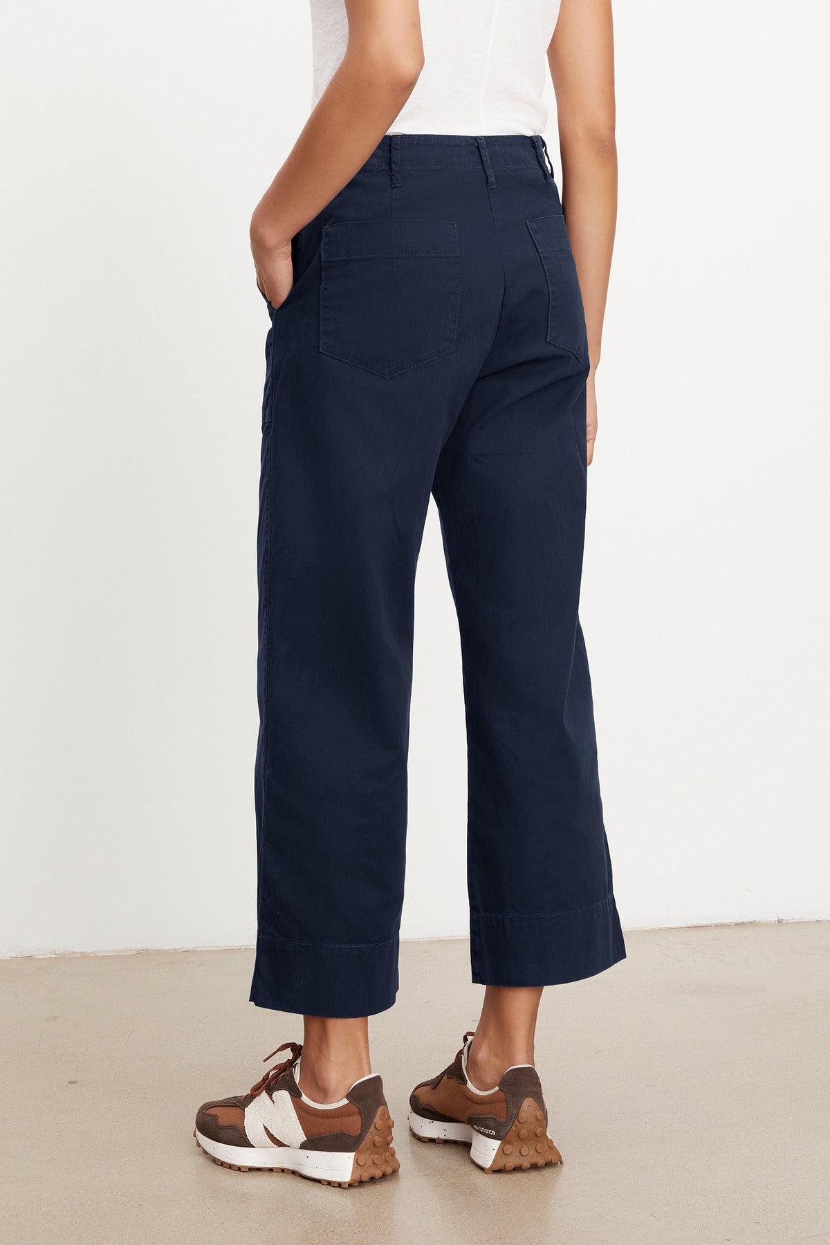 Rear view of a woman wearing Velvet by Graham & Spencer MYA COTTON CANVAS PANTS and brown chunky sneakers, standing on a plain background.-37628822487233