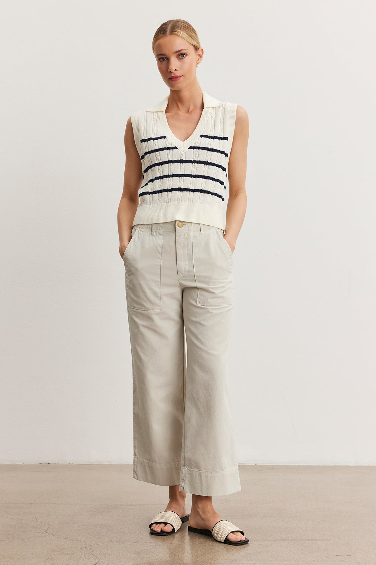   Woman in a sleeveless white top with blue stripes and light beige Velvet by Graham & Spencer MYA COTTON CANVAS PANT, standing in a studio, wearing black sandals. 