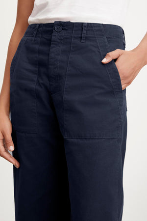 Close-up of a woman's hand touching the pocket of MYA COTTON CANVAS PANTS by Velvet by Graham & Spencer, highlighting the stitching and fabric texture.