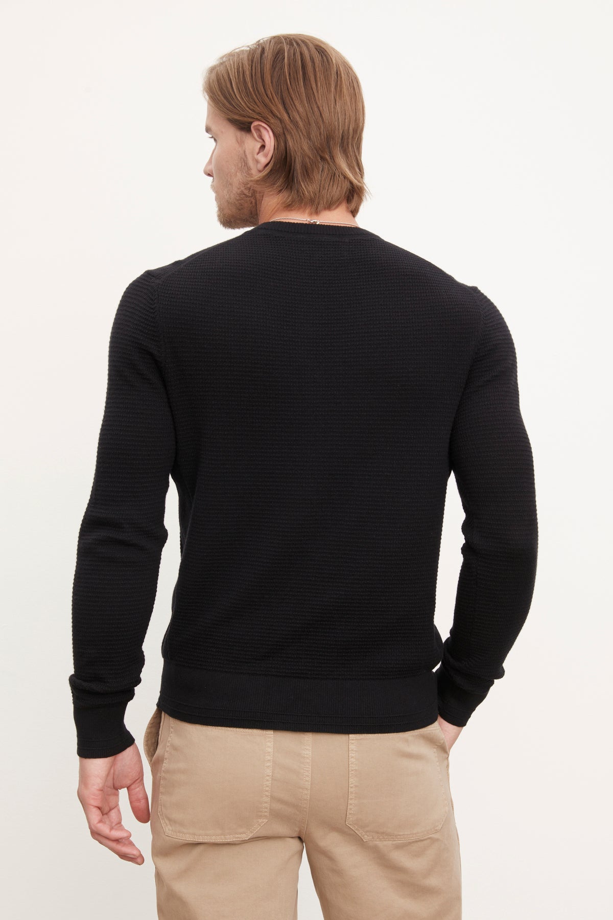   The back view of a man wearing a Velvet by Graham & Spencer ACE THERMAL CREW black sweater and khaki pants. 
